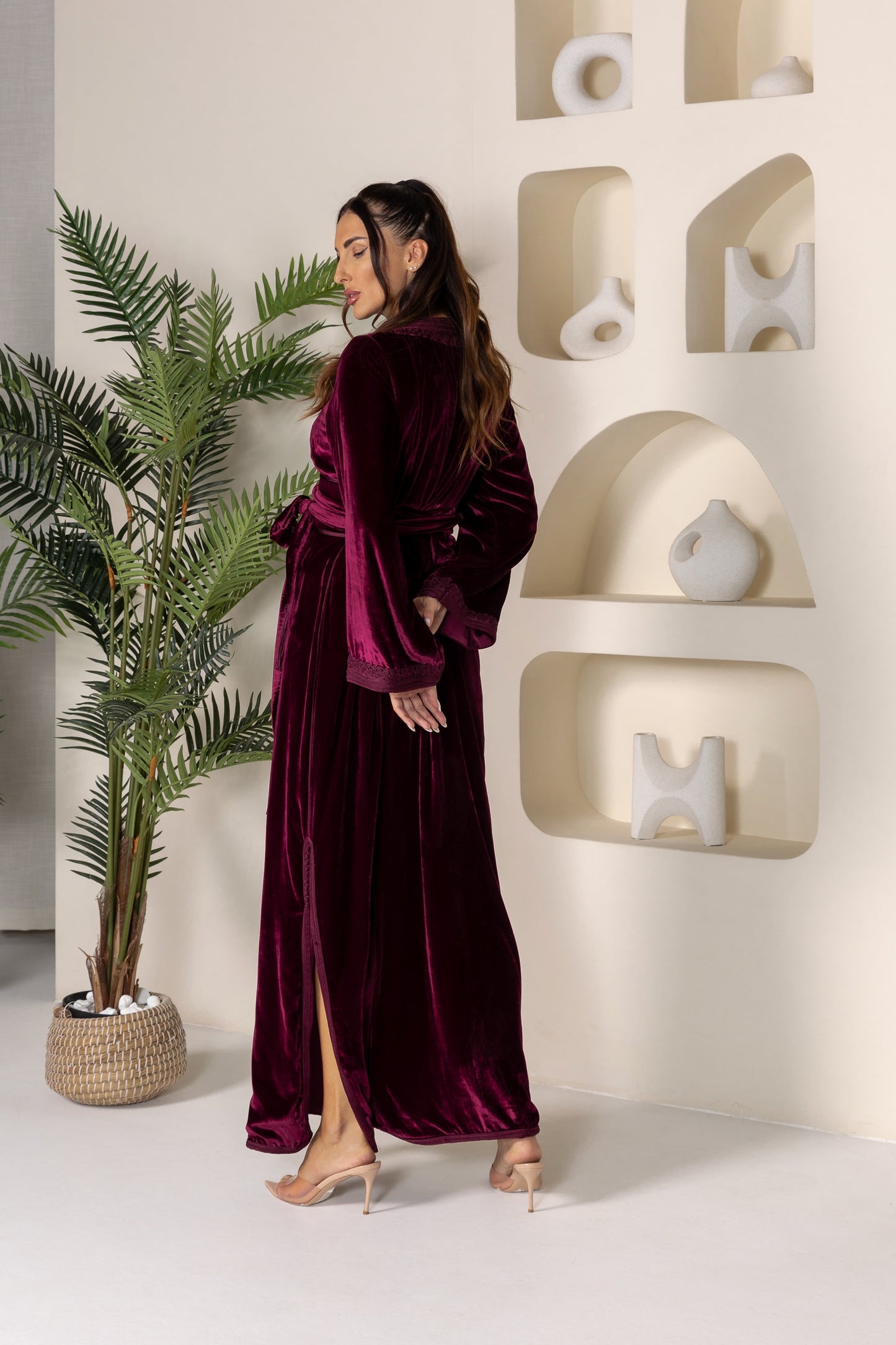 Back view of a maroon velvet Moroccan kaftan with flowy fabric and side slit