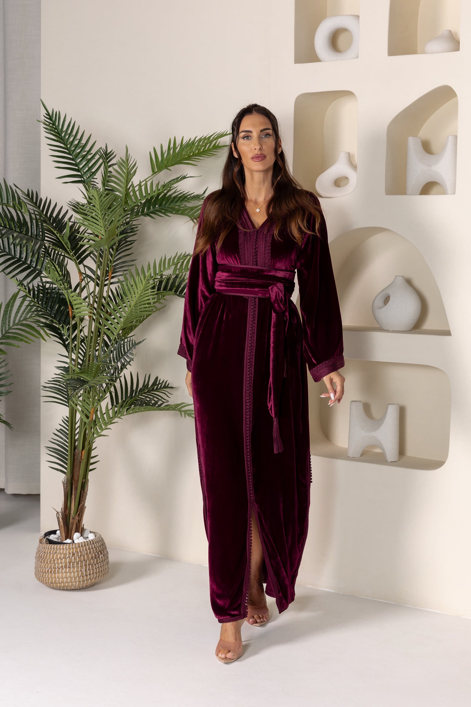 Woman in maroon velvet Moroccan kaftan with wide sleeves and a matching belt